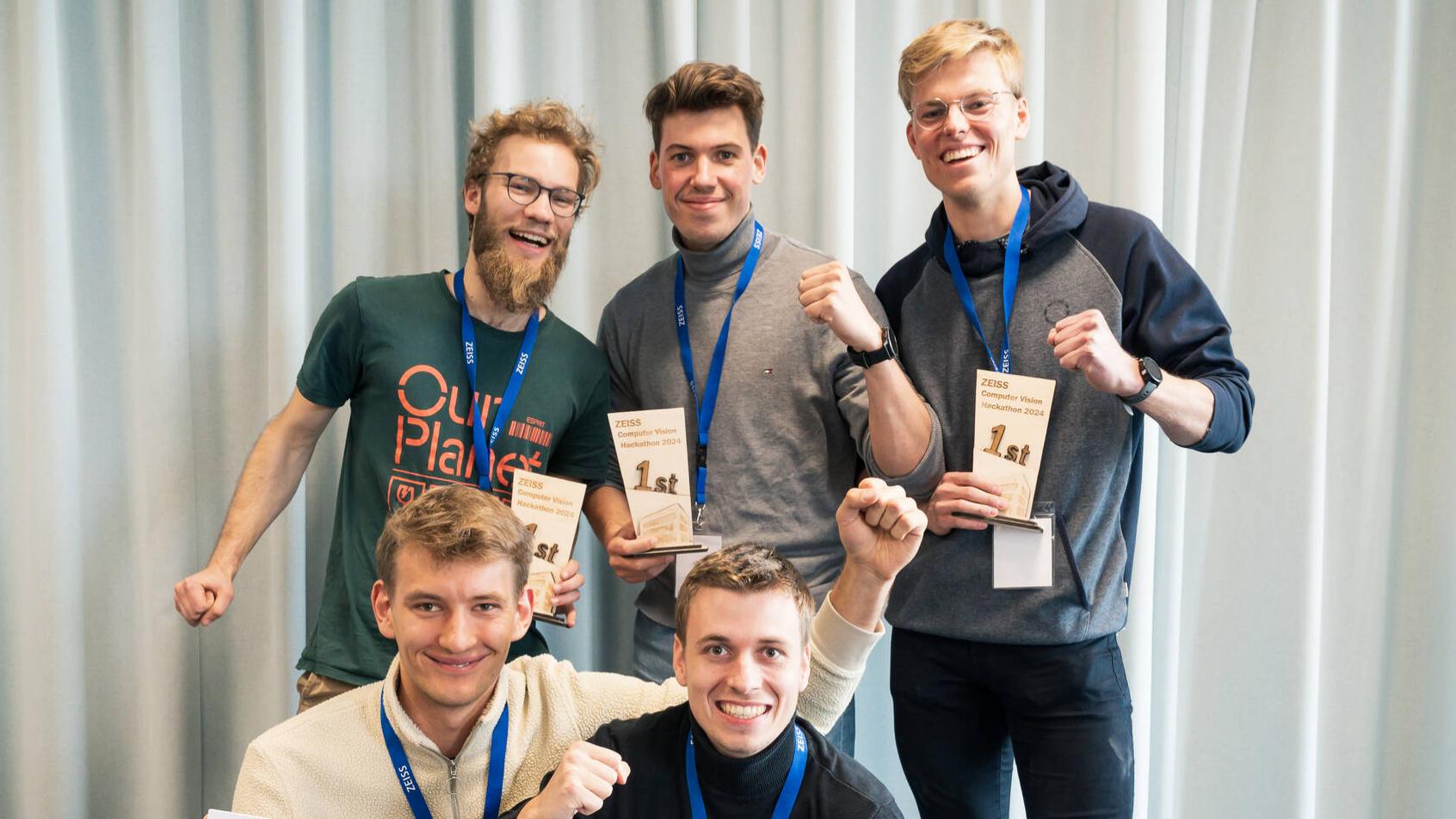 A group photo of the winner team of the ZEISS Computer Vision Hackathon 2024. Two of the five participants are holding a giant cheque