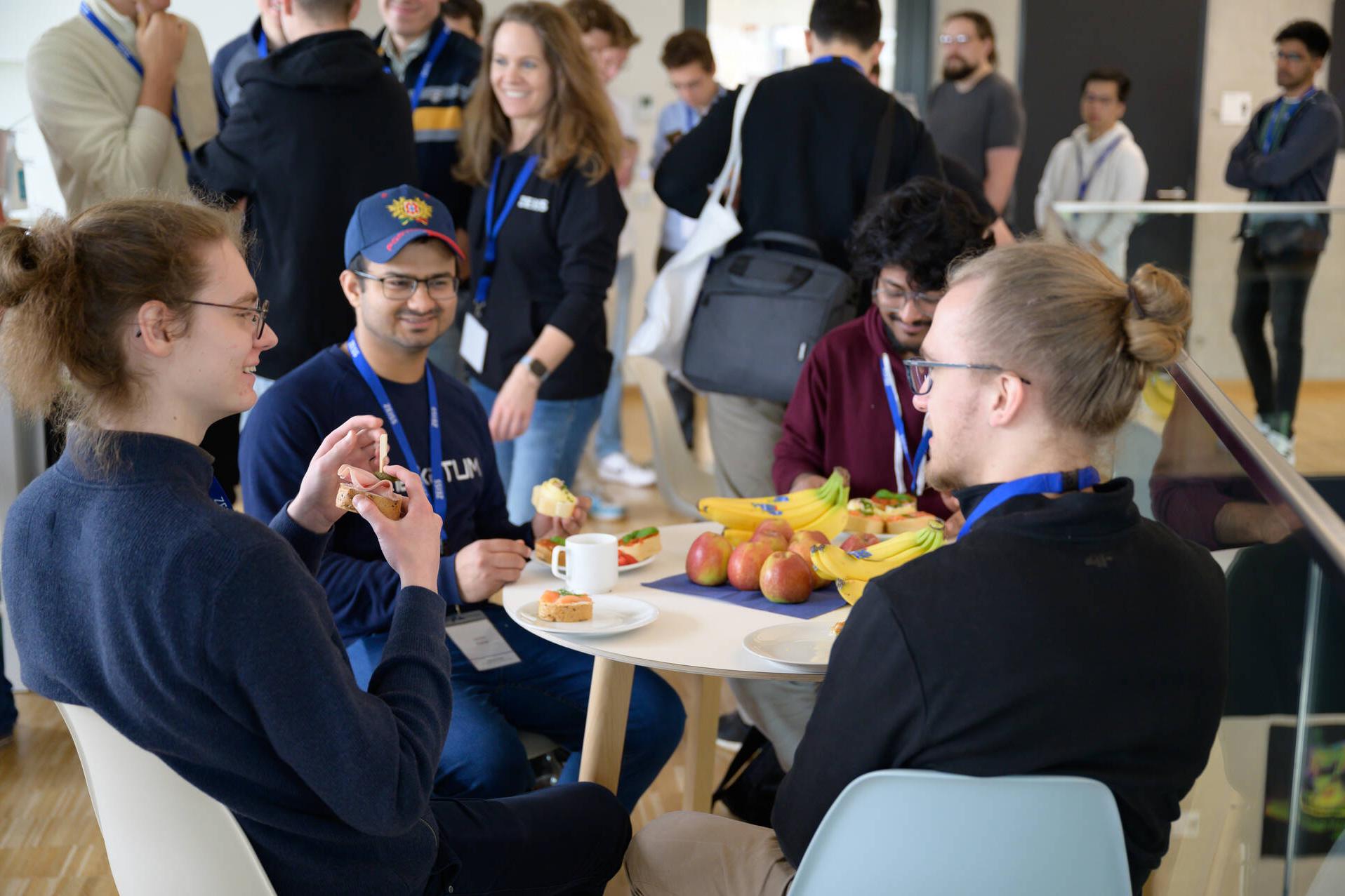 Four hackathon participants sitting around a table with coffee, snacks and fruit