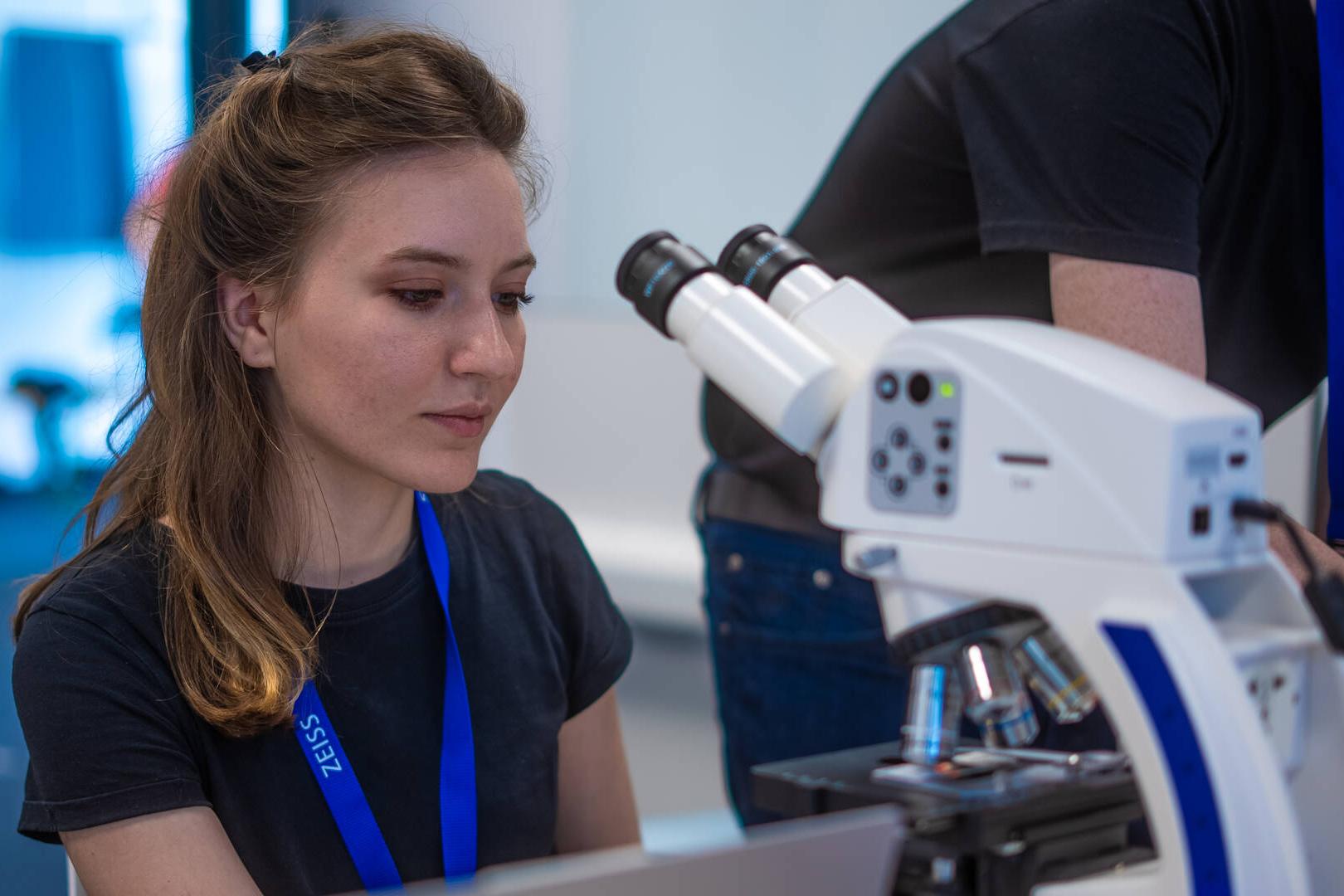 A participant of the ZEISS Computer Vision Hackathon 2024 sitting at a table in front of a microscope.