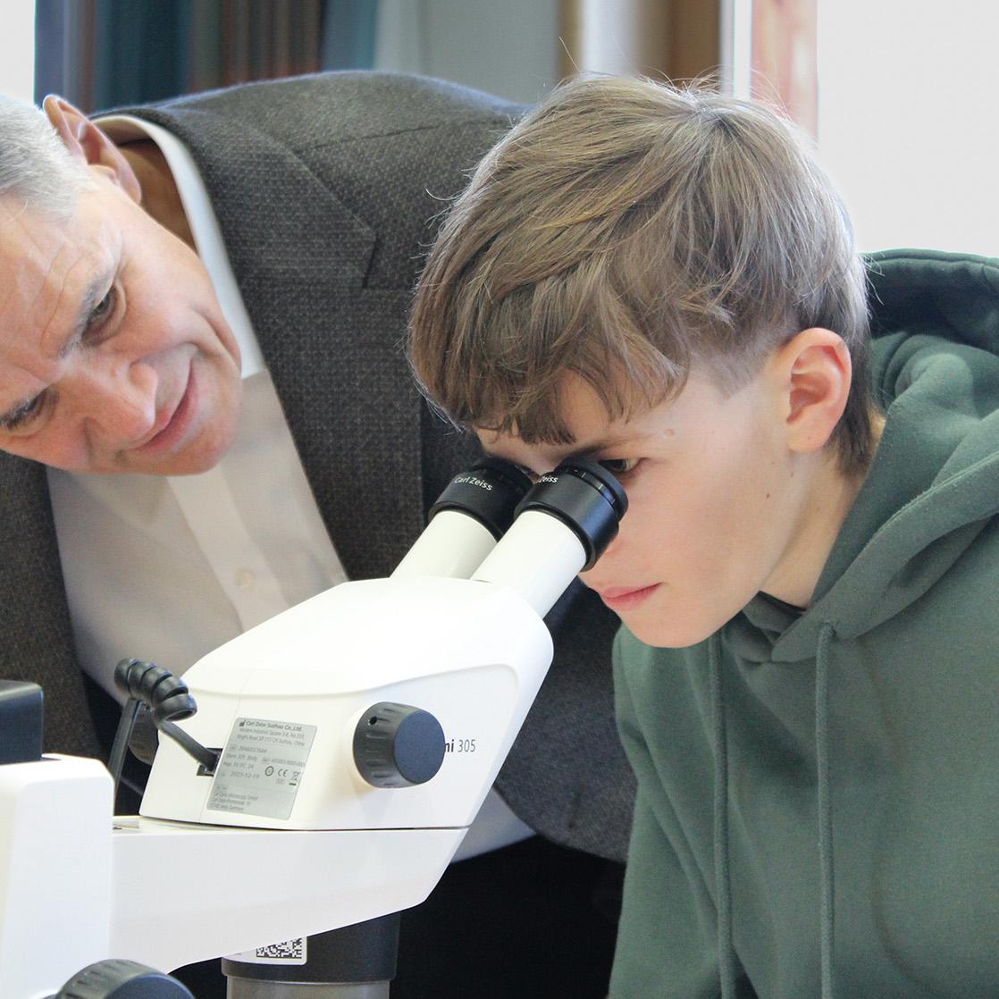 Karl Lamprecht is watching through a microscope with a kid