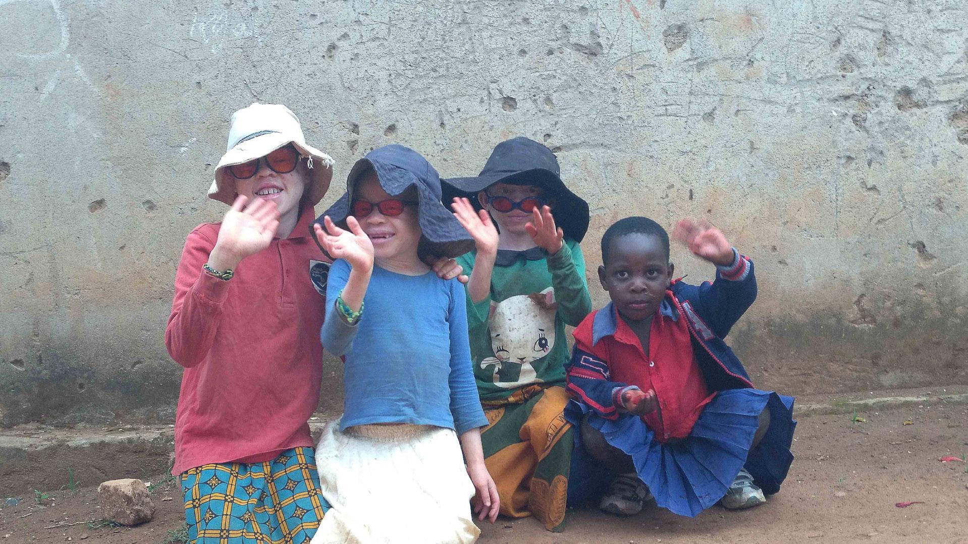 A group of children wave at the viewer's perspective