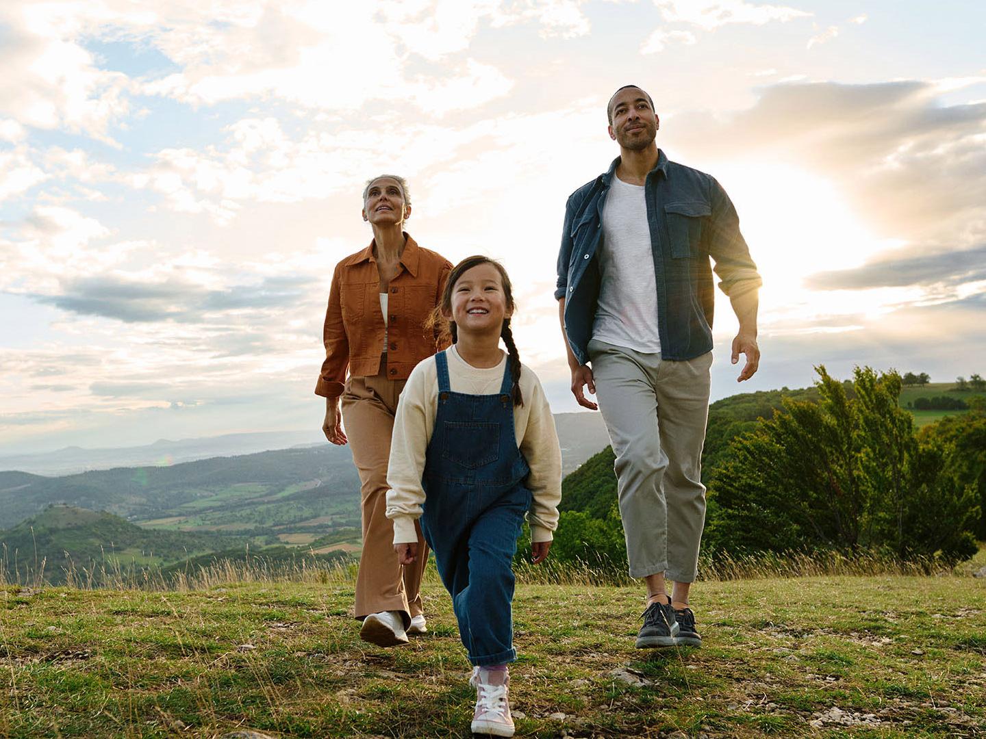 Ein Kind, eine Frau und ein Mann laufen gemeinsam durch eine grüne Naturlandschaft