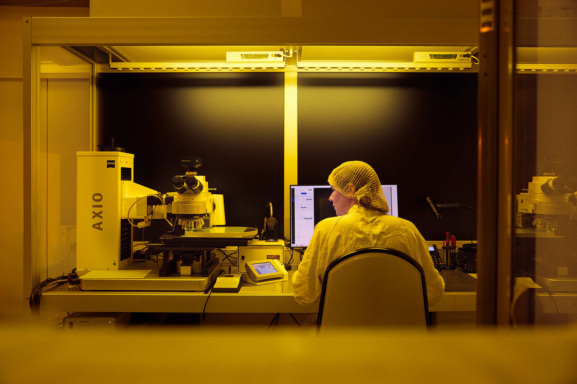 A man in protective clothing sits in a laboratory with yellow lighting and looks at a device.