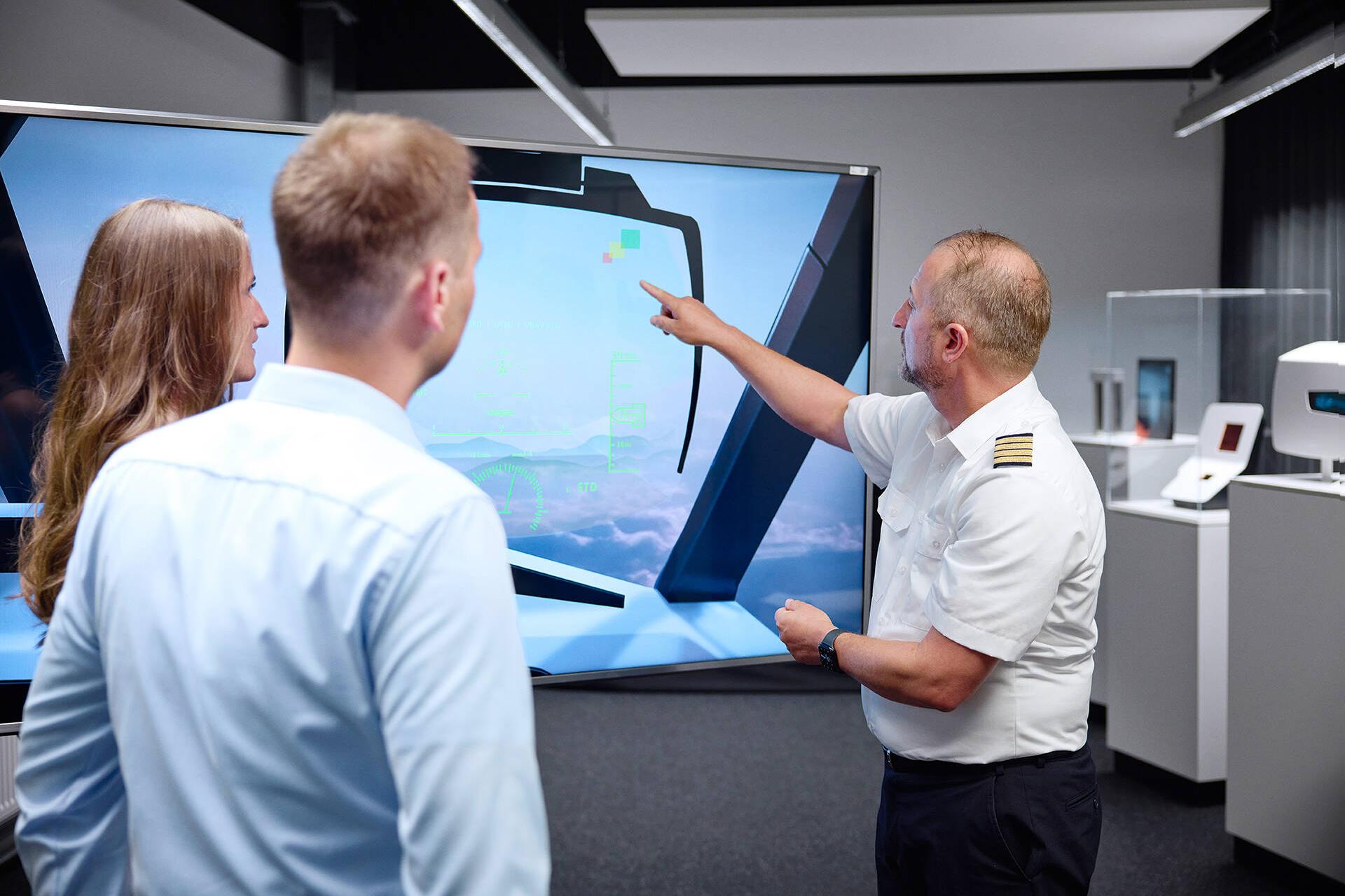 Commercial pilot Tino Janke shows Linda and Dennis a model of a head-up display that projects important information directly into their field of vision thanks to augmented reality.