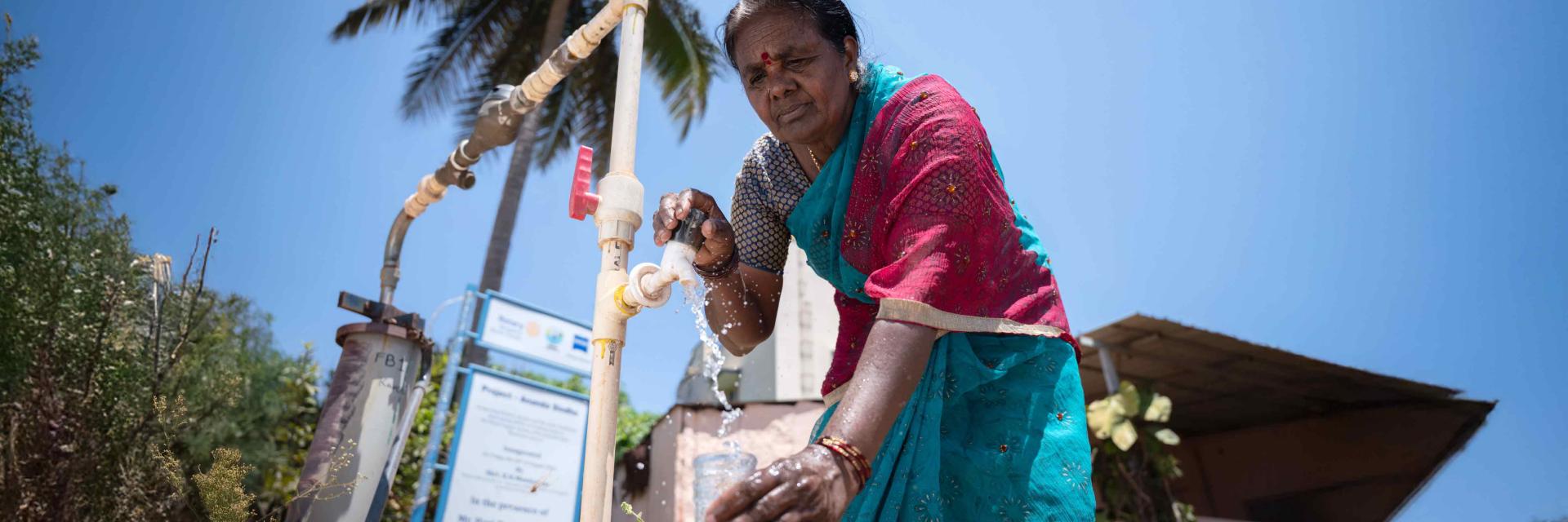 A woman pours water from a tap into a vessel.
