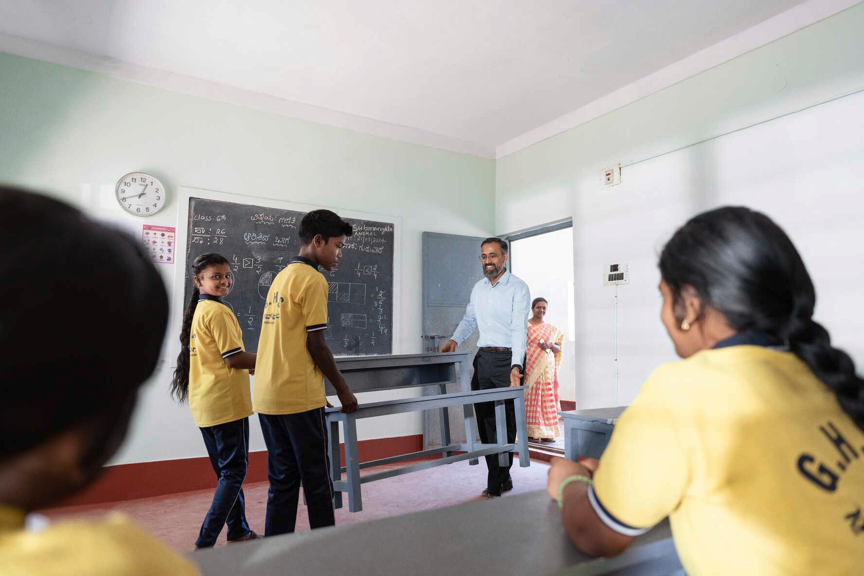 Pupils are helping Manoj Sharma carry new benches into a classroom