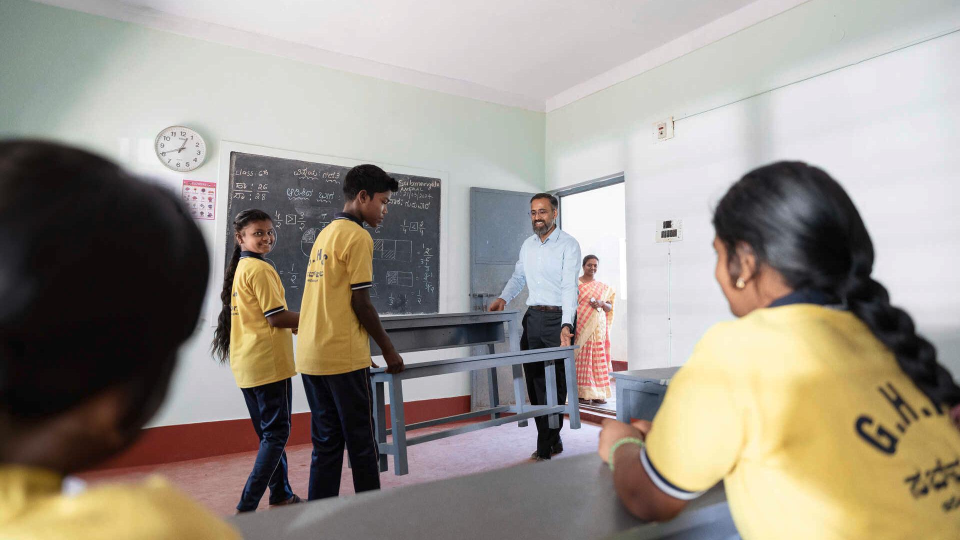 School children and Manoj Sharma carry new school desks into a classroom