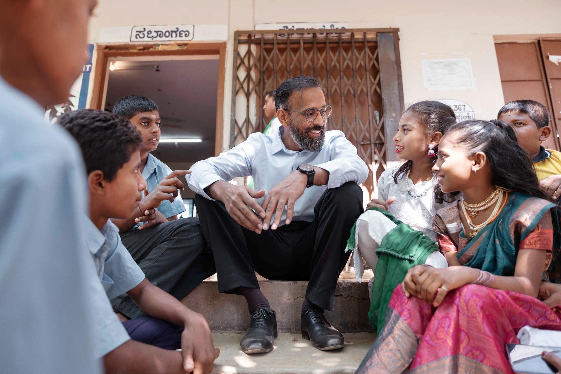Manoj Sharma sits on stairs in front of a school surrounded by pupils