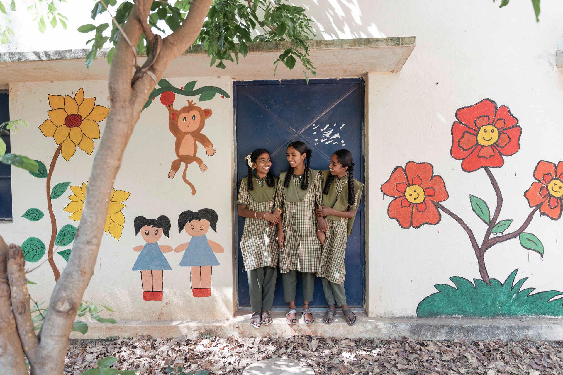 Three children are standing in a doorway of a colorfully painted school building