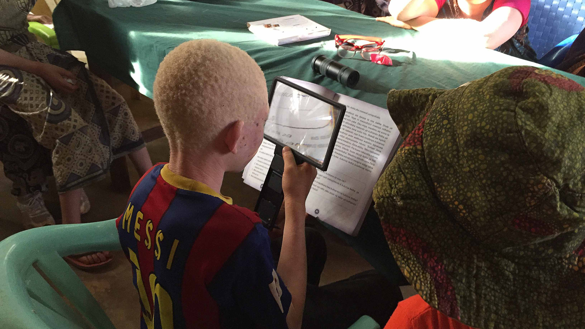 A boy with albinism trying to read a school book with a special visual aid.