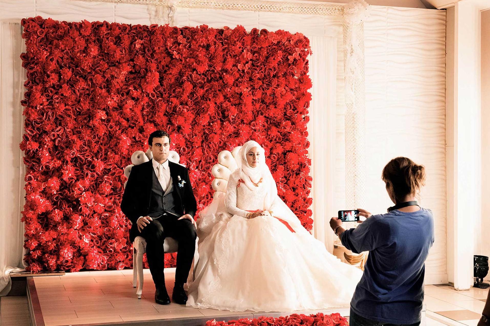 Sherry Hormann taking picture of bridal couple in front of wall of flowers
