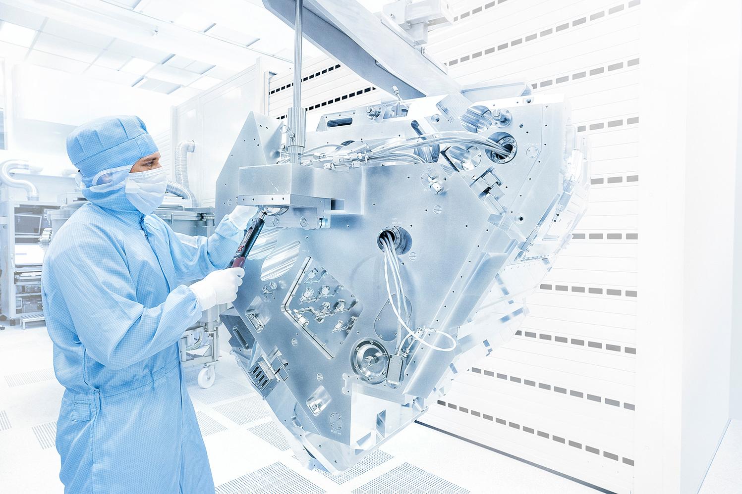 ZEISS employee in light blue cleanroom clothing stands next to machines for EUV technology.