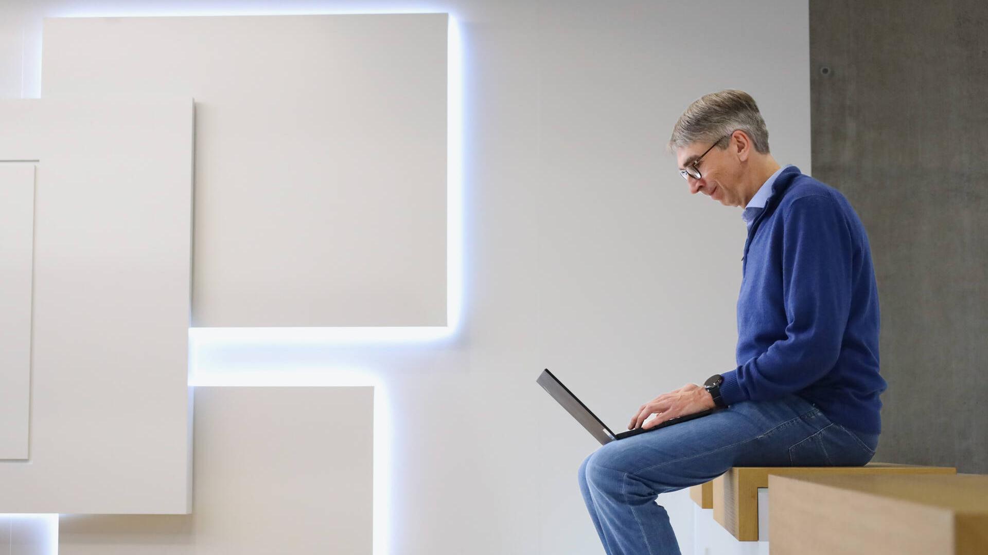 Dr. Ulf Wilhelm sitting on a wooden bench in a community space at work.