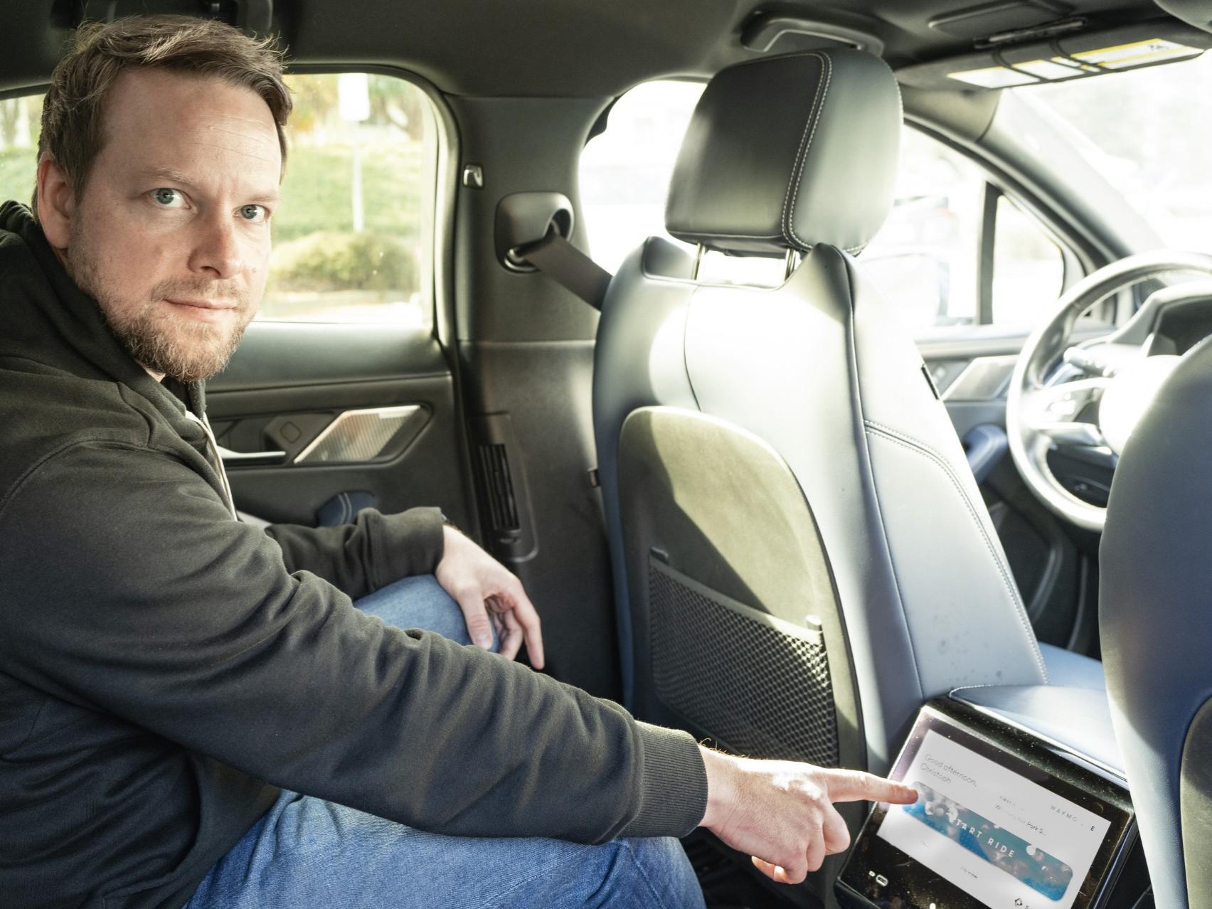 Christoph sitzt auf dem Rücksitz und nutzt das Passagierdisplay des Taxis.