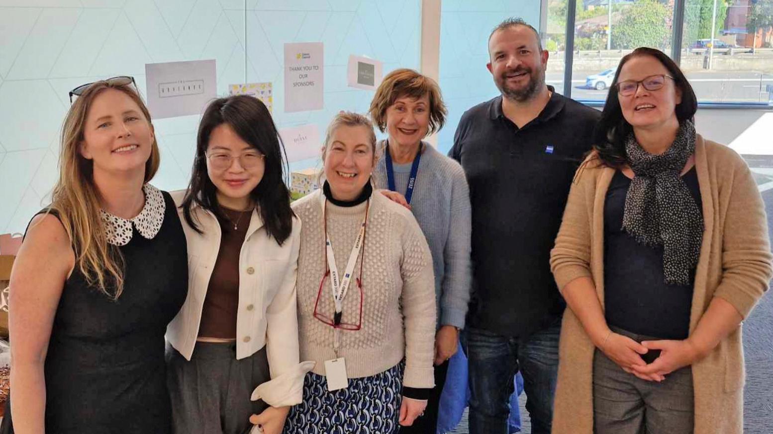 From left to right: Taegan Guthridge, Linh Doan, Vivien Ferizis, Juanita Clare, Wayne Gauci, and Ines Seringer at the Sydney location. They are all smiling at the camera.