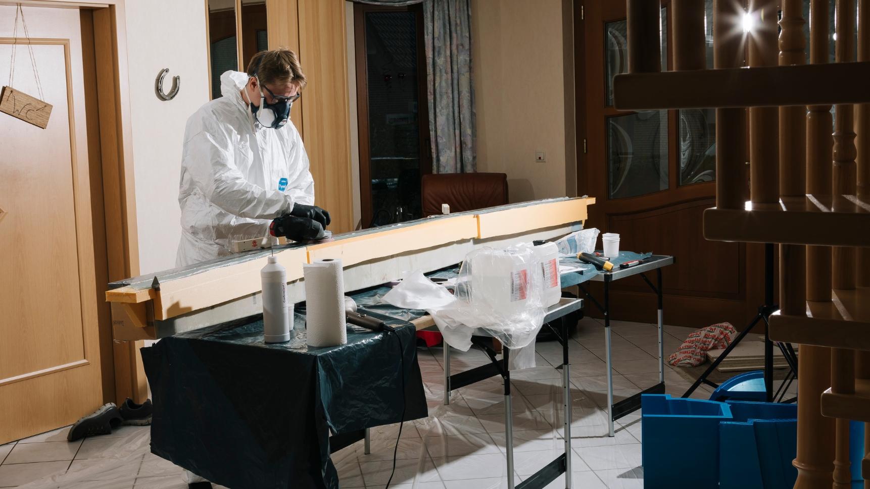 Eine Person in Schutzkleidung arbeitet in einer Werkstatt an Laminier- und Schleifarbeiten für Flugzeugteile.