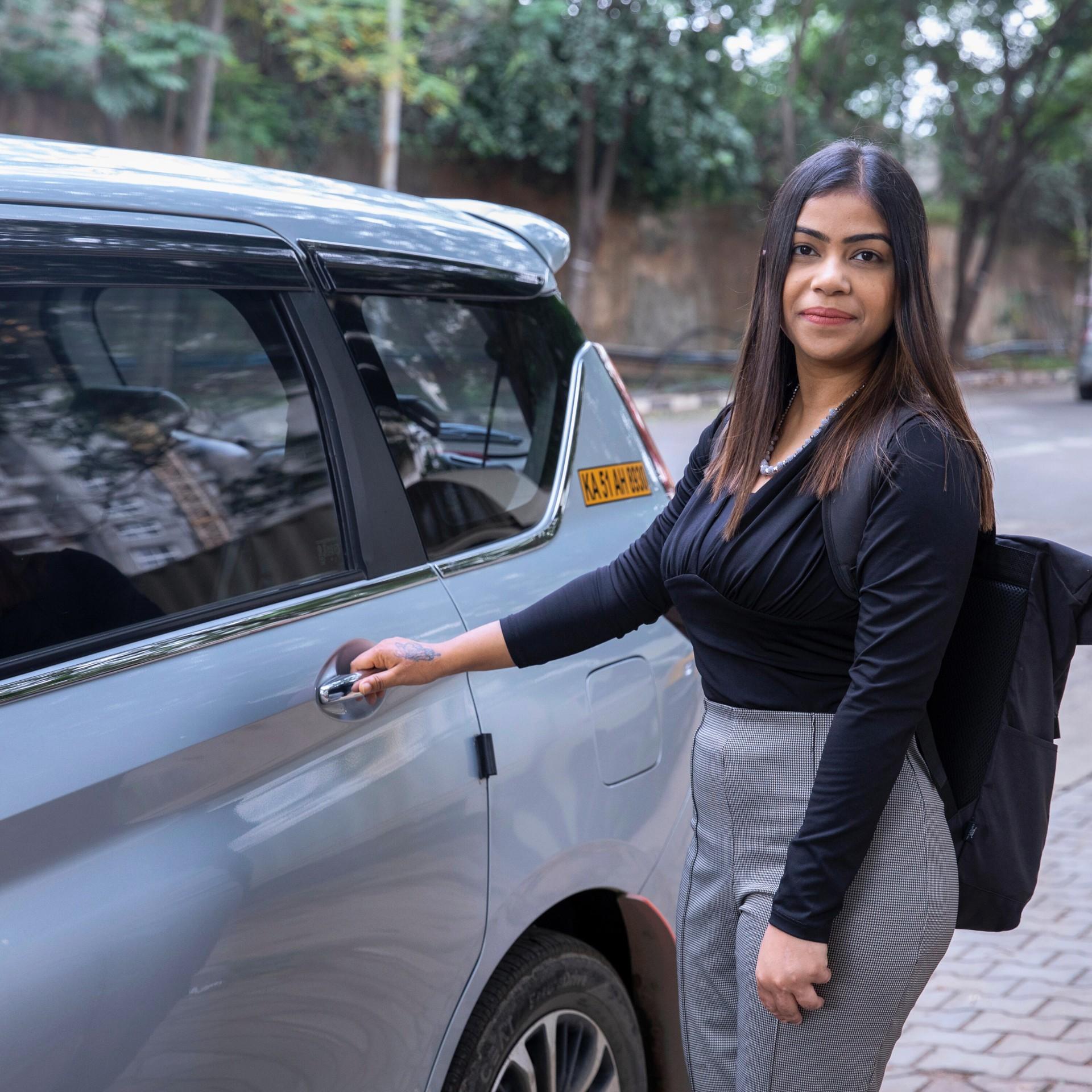 Kajal Kamal steht an einem Auto, hält ihre Hand am Türgriff und lächelt freundlich in die Kamera.