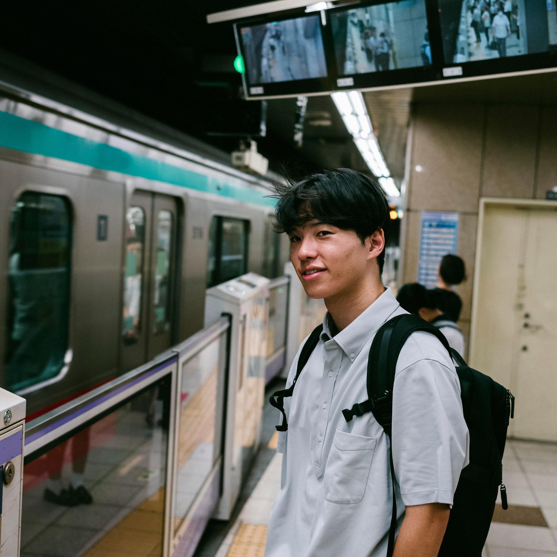 Sonoda Takuto steht an einer U-Bahn-Haltestelle, bereit, in einen Zug einzusteigen.