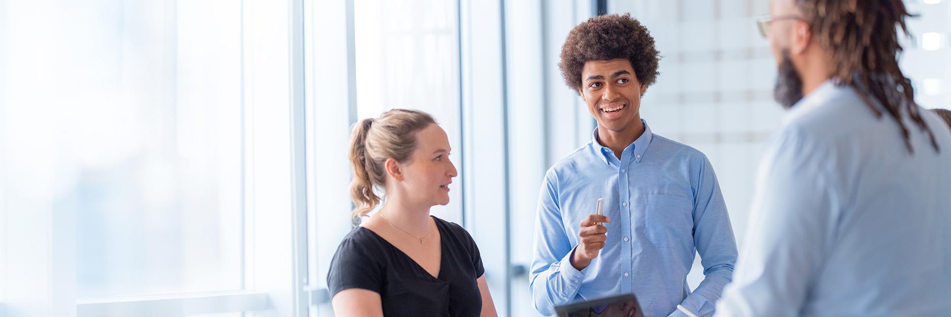 Three people stand at a desk in a modern office and chat.