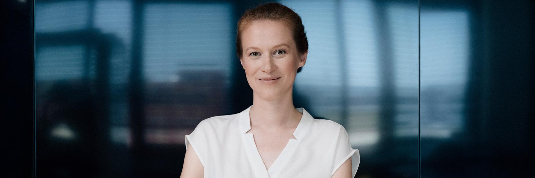 Franziska steht vor einer dunklen, modernen Glaswand. Sie blickt ruhig und selbstbewusst in die Kamera, während sie die Arme verschränkt hält.