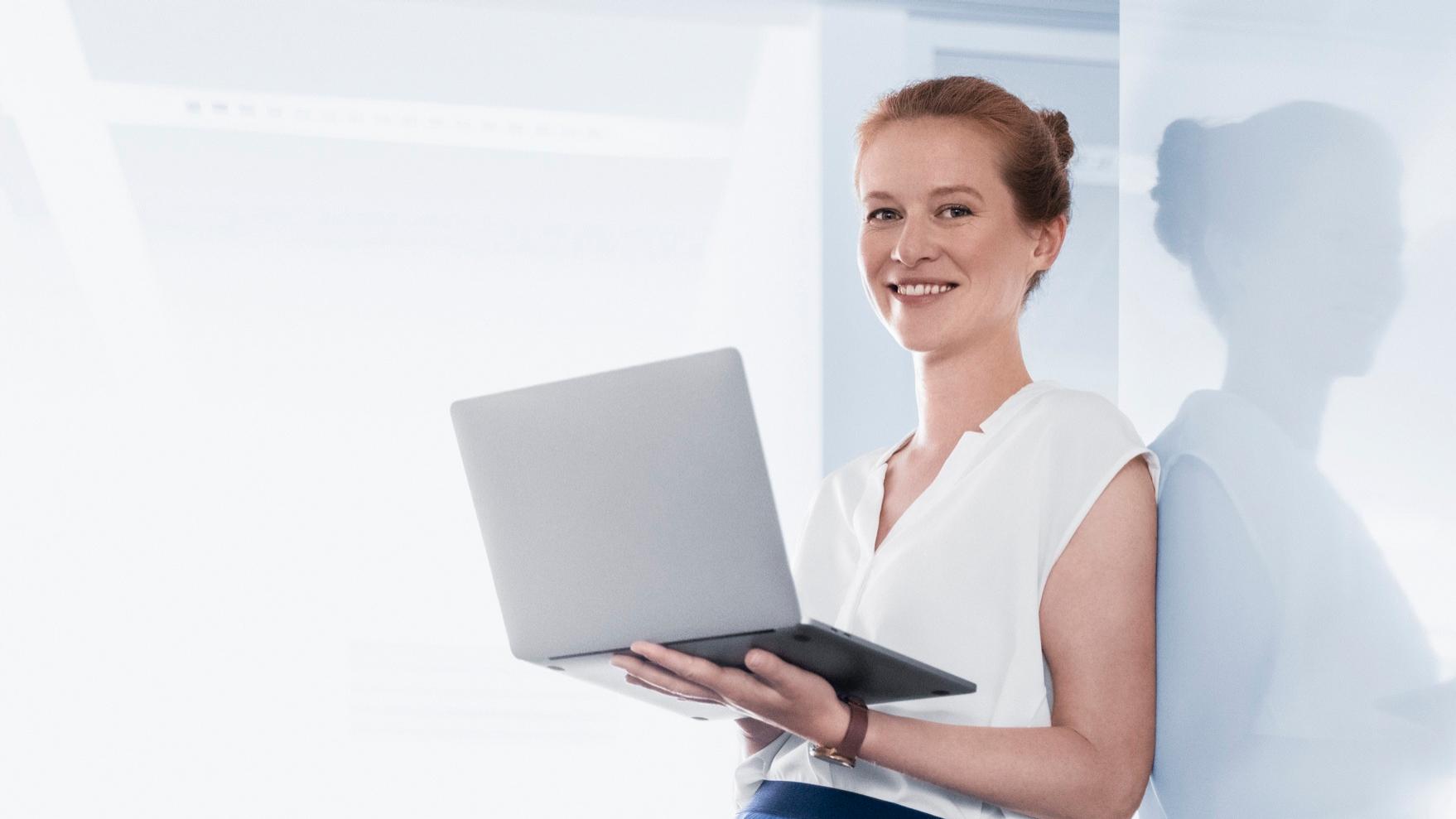 Franziska stands in a bright room. She holds a laptop in her hand and looks at the camera.