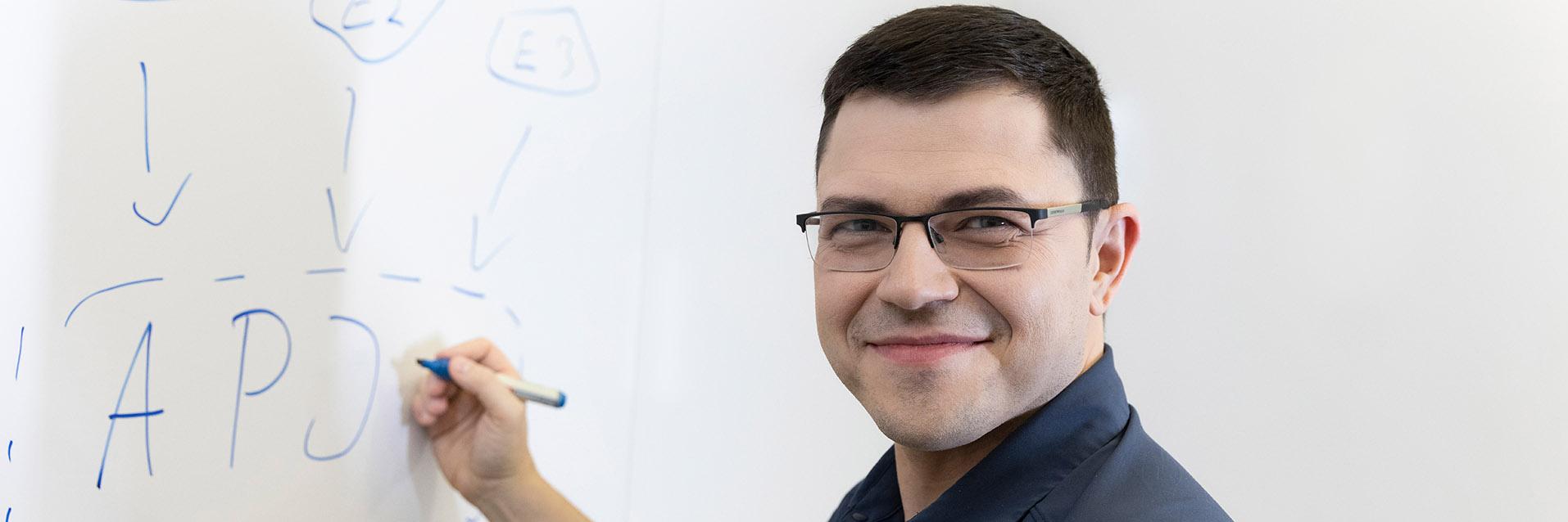 Hendrik stands in front of the whiteboard with a marker pen in his hand, while looking warmly at the camera.