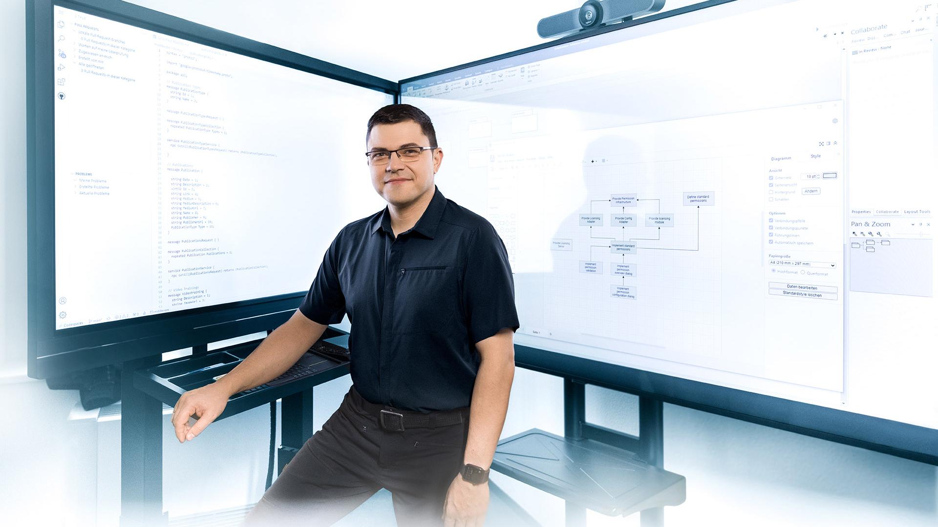 Hendrik stands in front of two large screens displaying technical diagrams and code.
