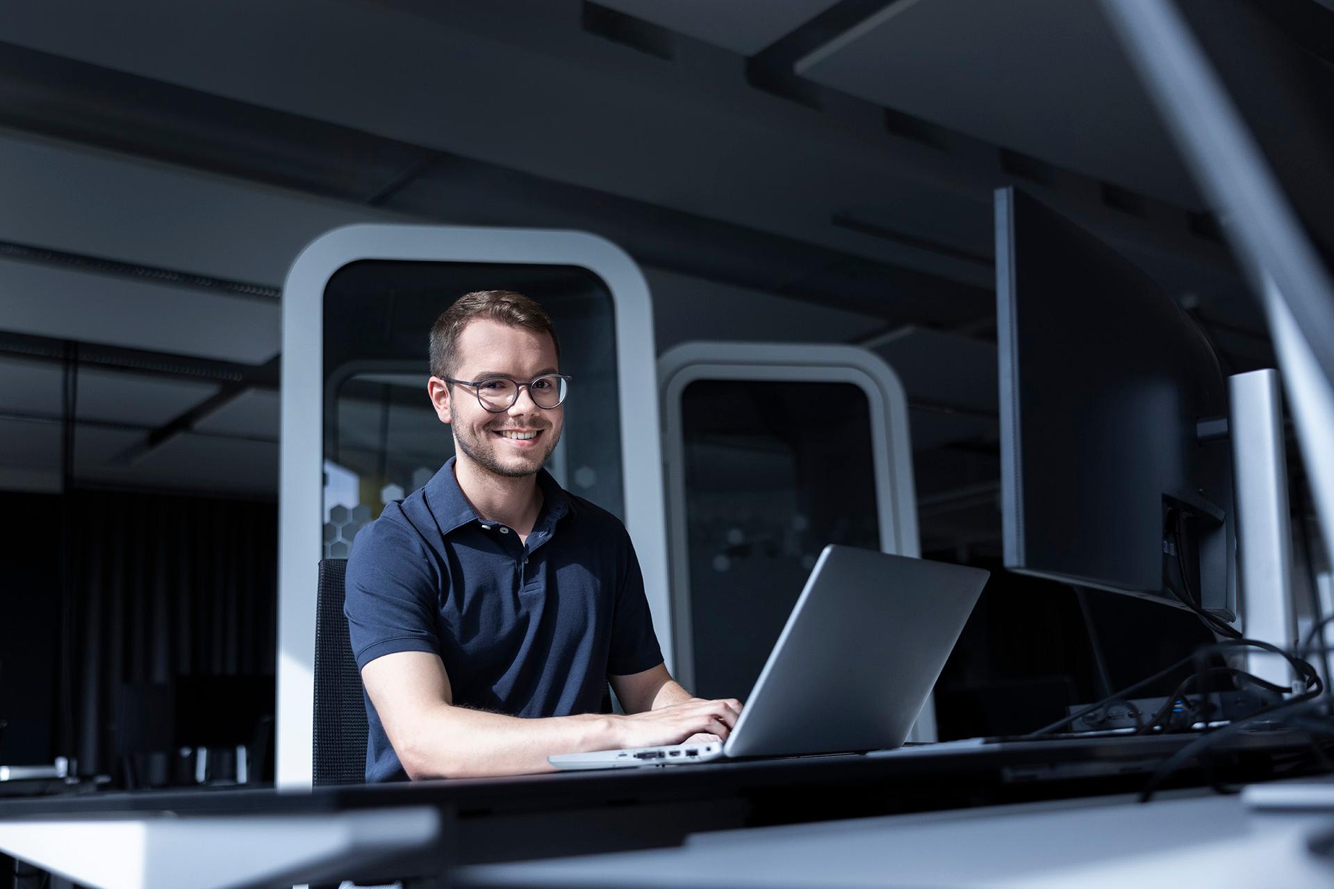 Julian, an employee, is sitting at a laptop, grinning and typing on the keyboard.