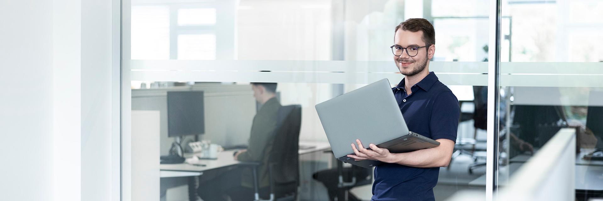 Julian is standing in his office with his opened laptop and is carefully checking some of the data on the screen.