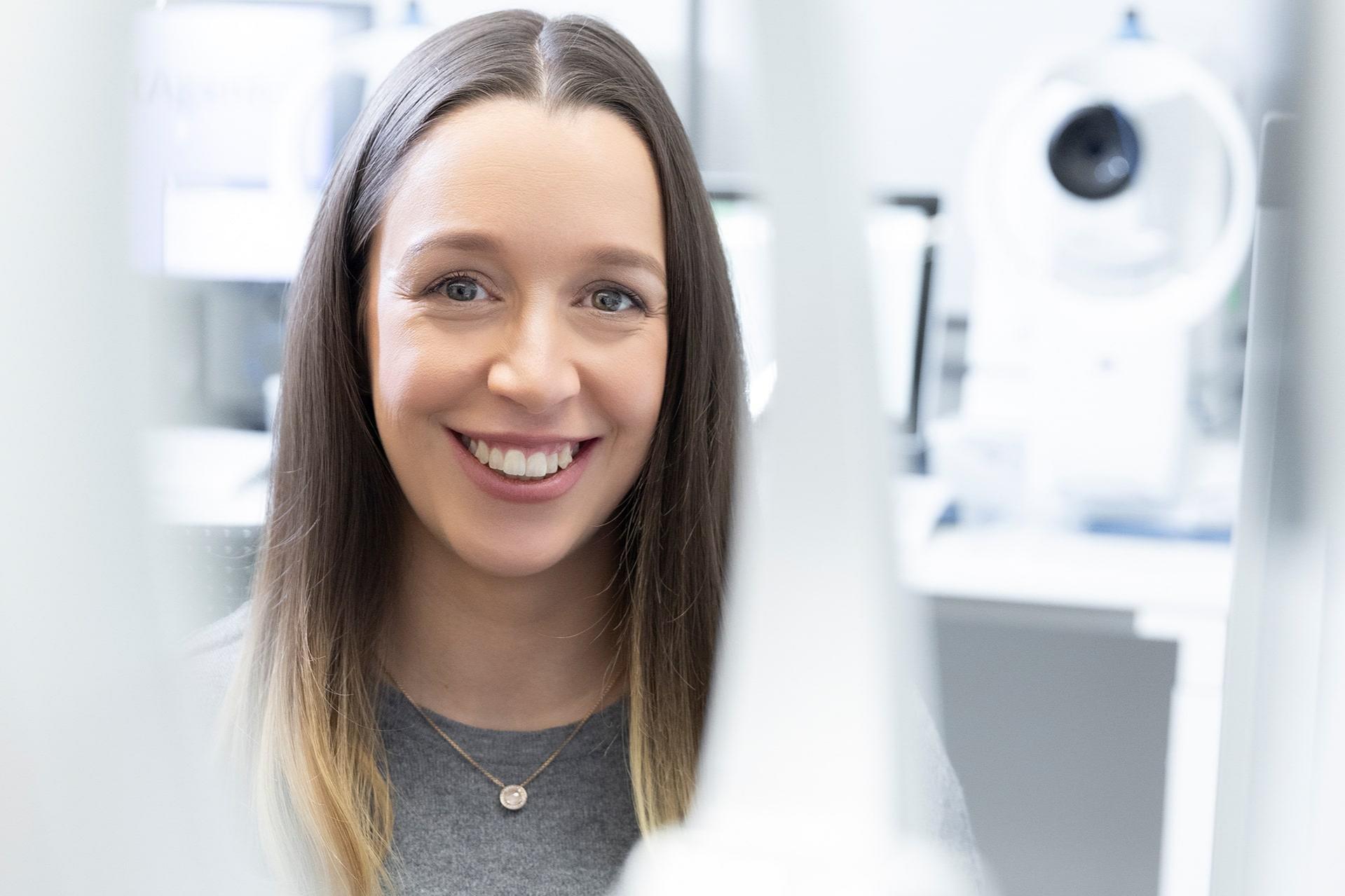 Karolin looks warmly at the camera. A modern office with ZEISS equipment can be seen in the background
