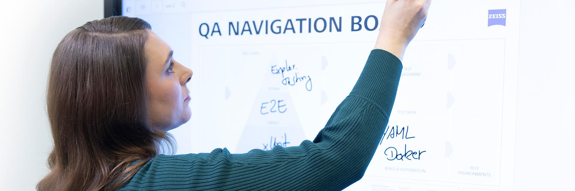 Maria stands in front of a digital whiteboard and writes notes on the presentation with a marker pen.
