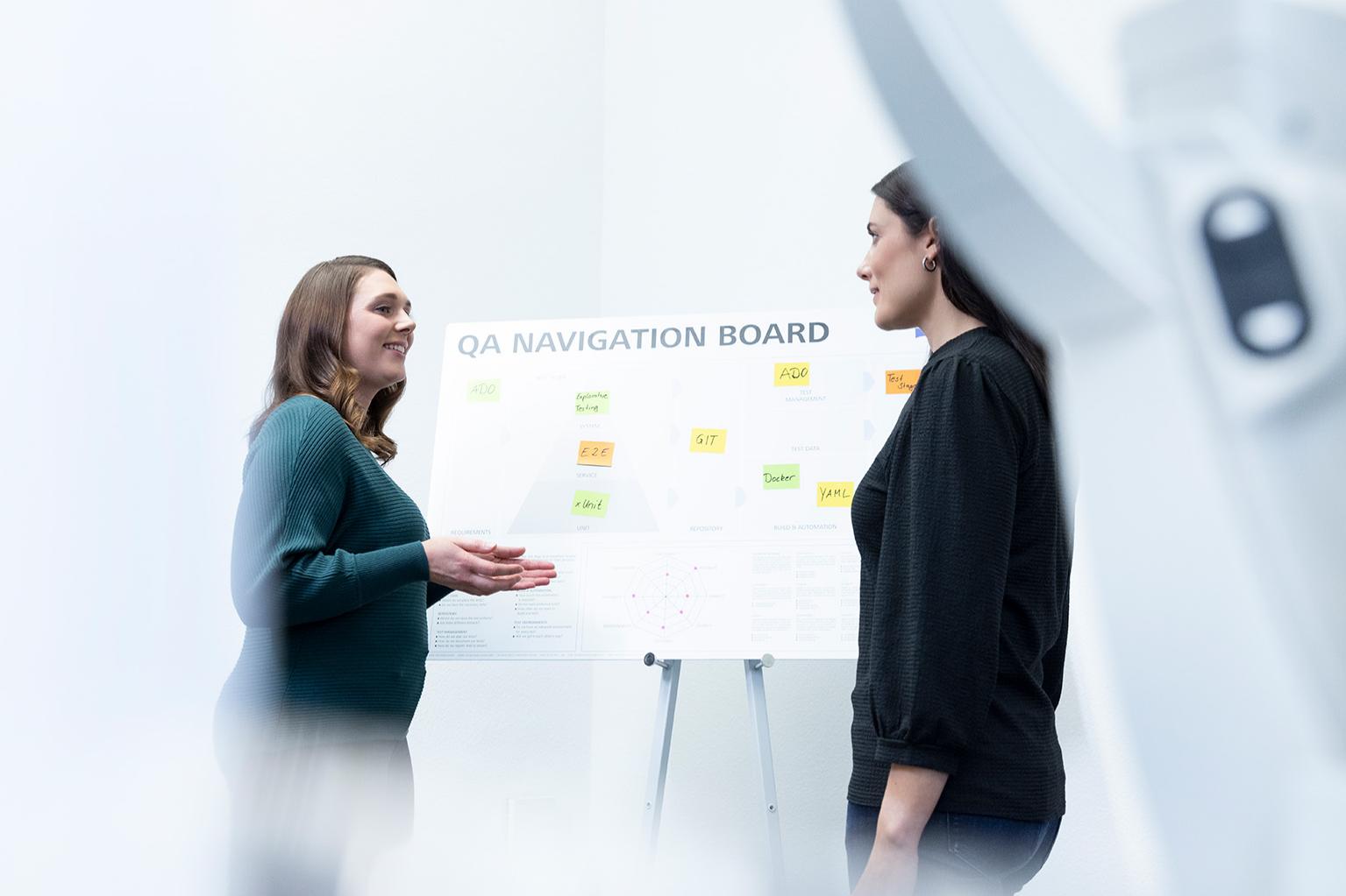 Maria chats to a female colleague in front of the QA Navigation Board