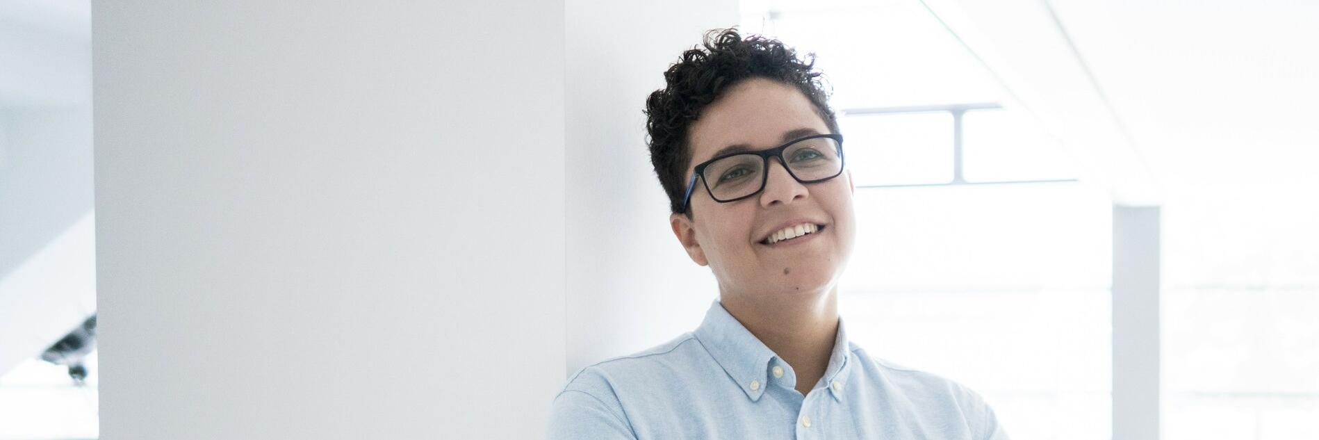 Nathalia steht in einem hellen Raum, blickt nachdenklich in die Ferne, während sie die Arme verschränkt hält