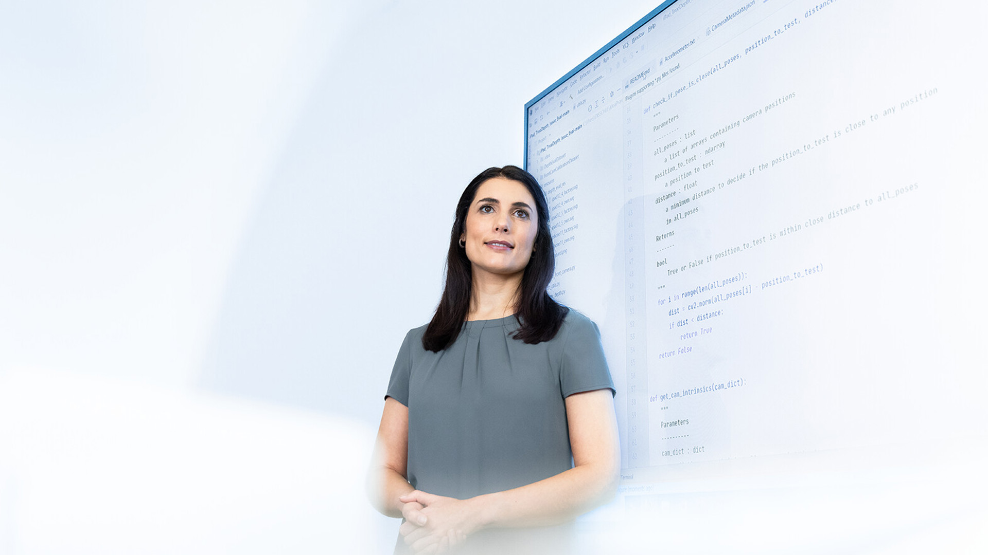 Sabrina stands in front of a large screen displaying program code