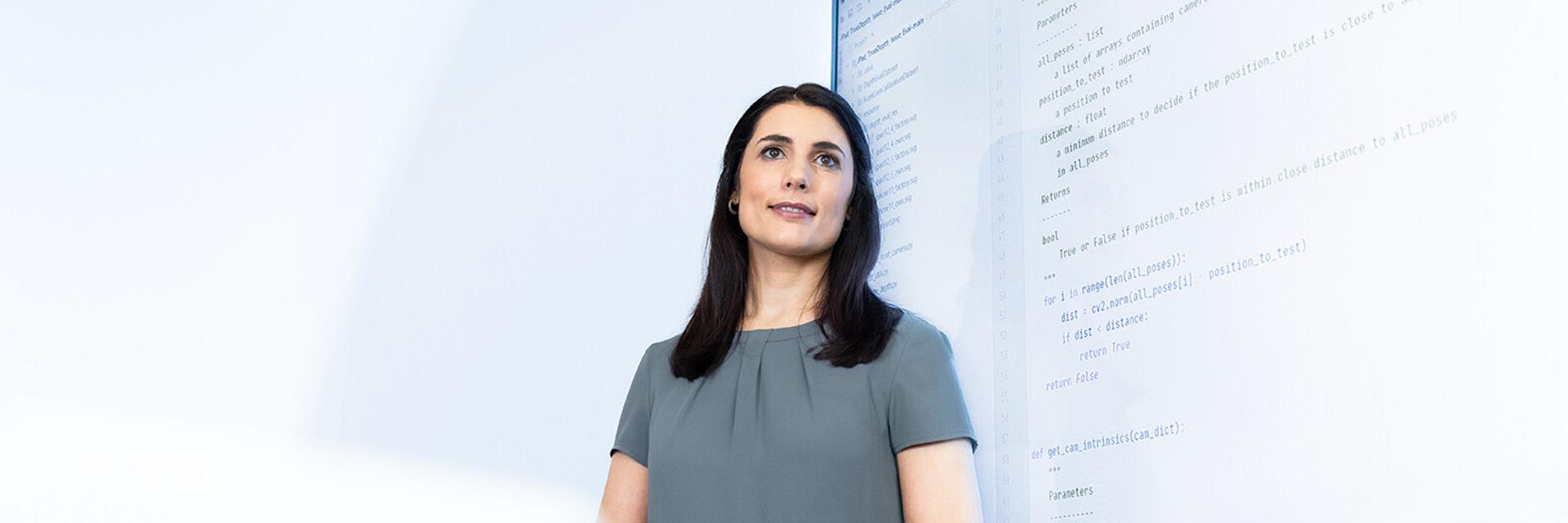 Sabrina stands in front of a large screen displaying program code