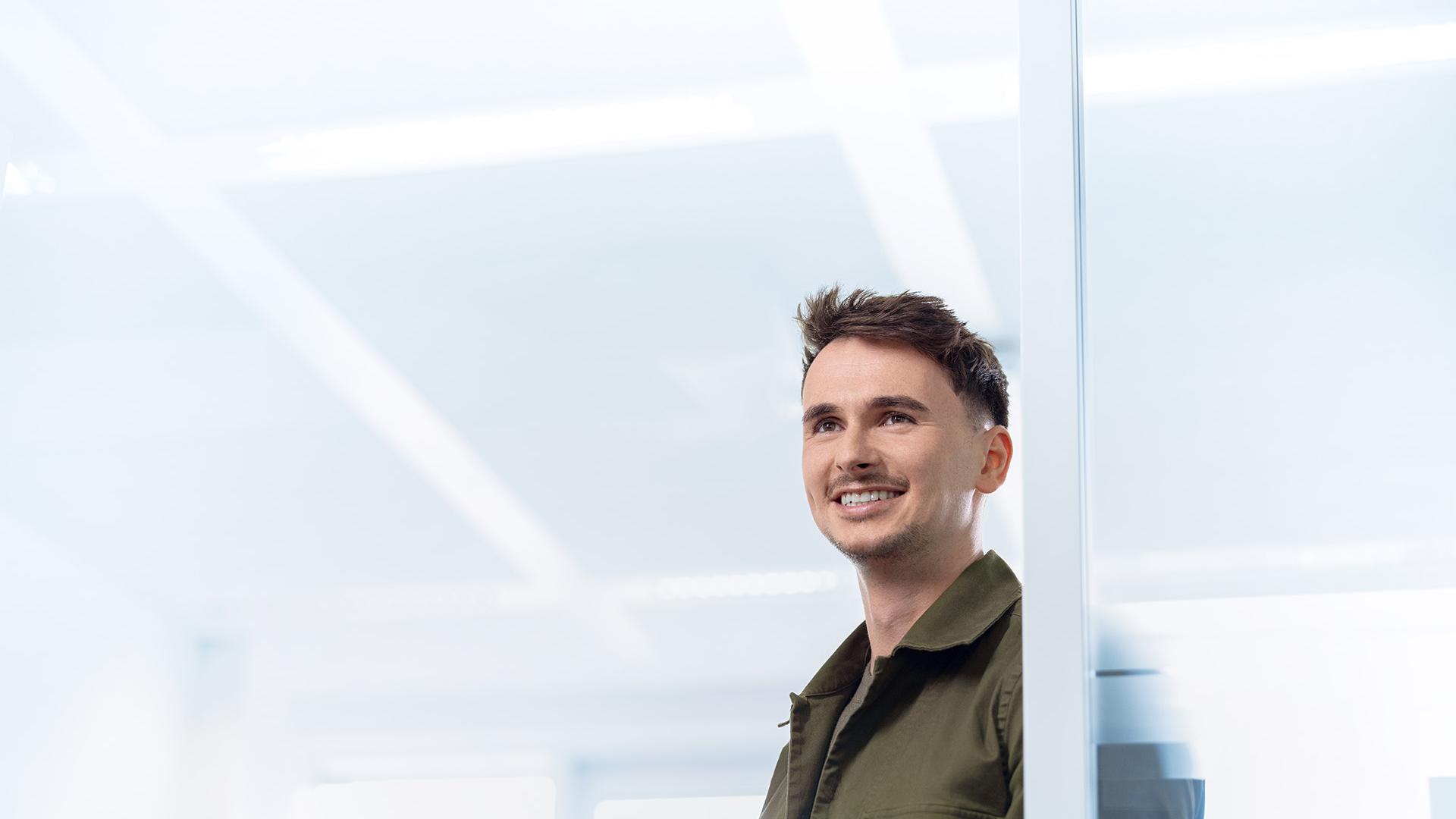 Simon is looking relaxed as he leans against the glass door to his office and looks into the corridor.