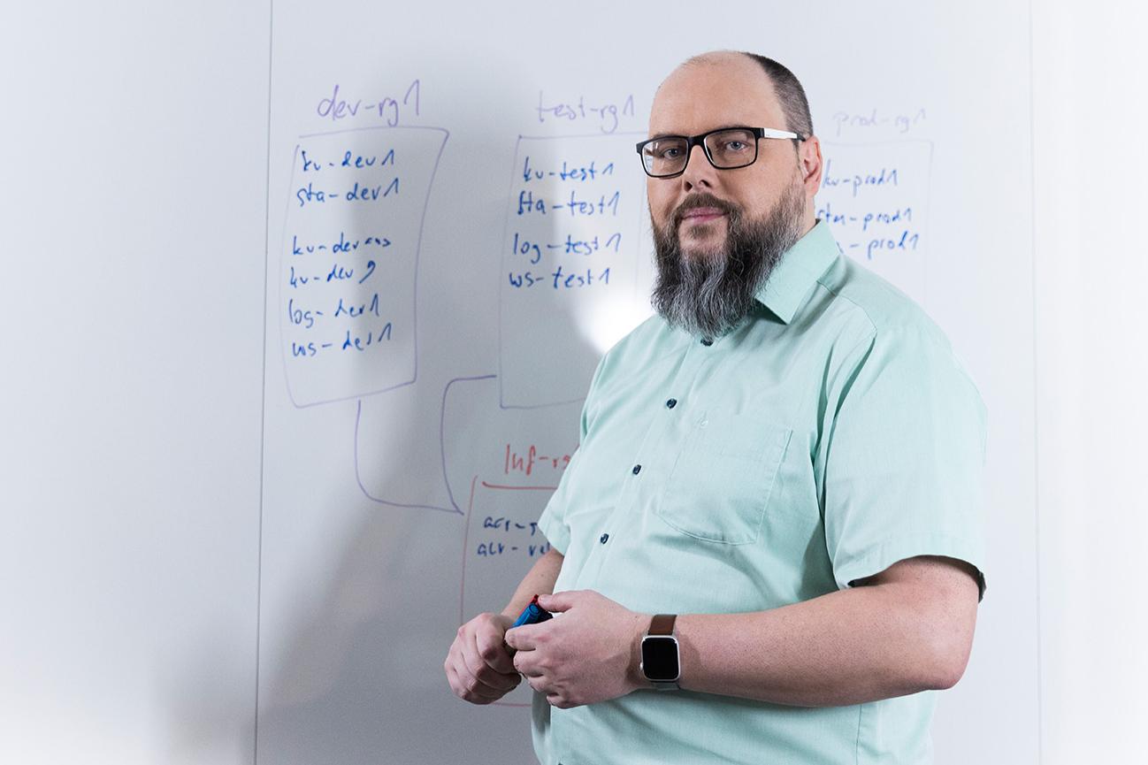 Sven stands in front of a whiteboard. He gesticulates as he explains the content of the notes written on the board to his male colleague