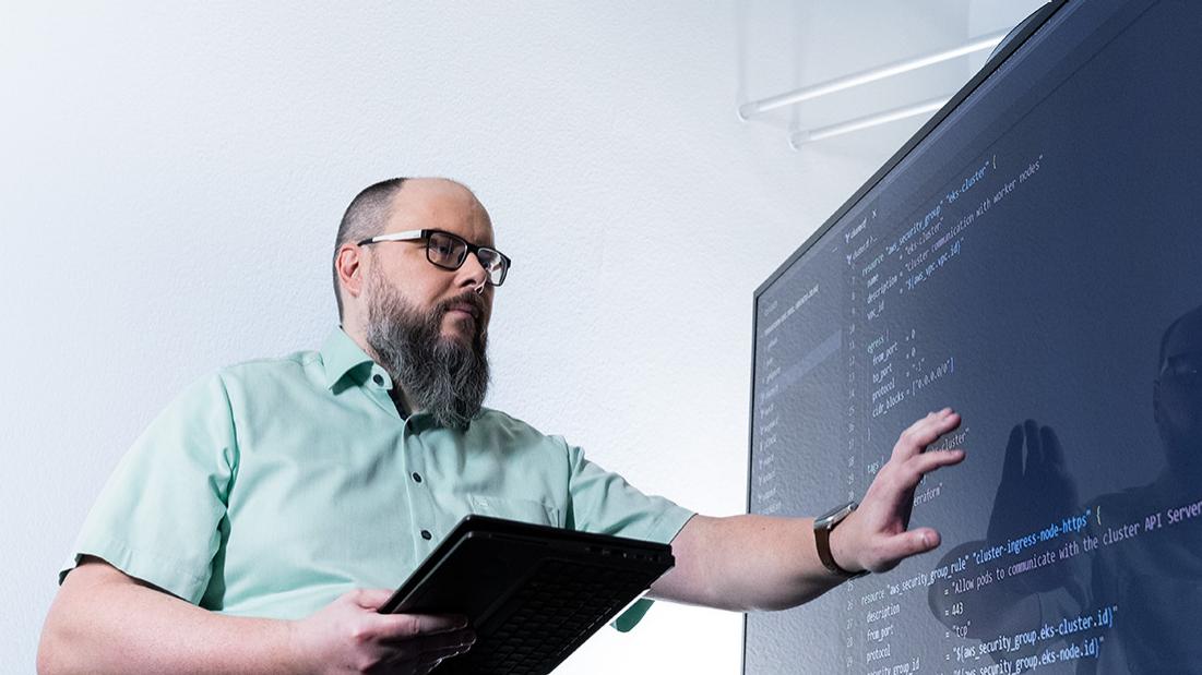 Sven steht vor einem großen Bildschirm, auf dem Programmcode angezeigt wird.