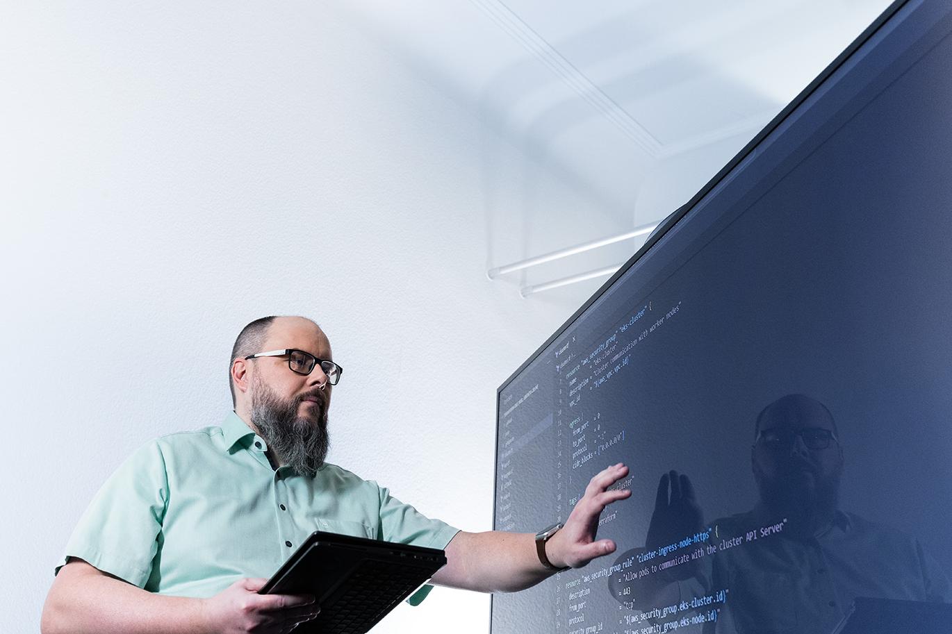 Sven stands in front of a digital whiteboard and works on program code