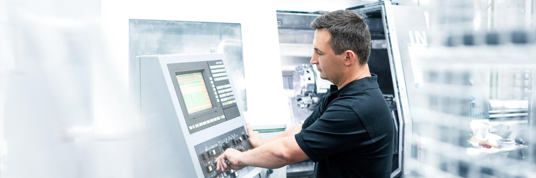 Waldemar steht neben einem Steuerungspult und bedient eine metallverarbeitenden Maschine
