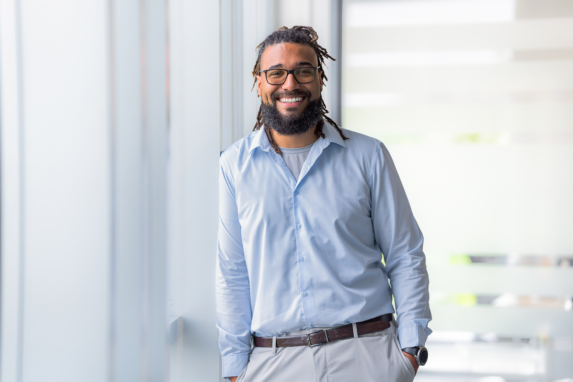 A relaxed Aaron smiles at the camera as he leans against a window in a ZEISS office.