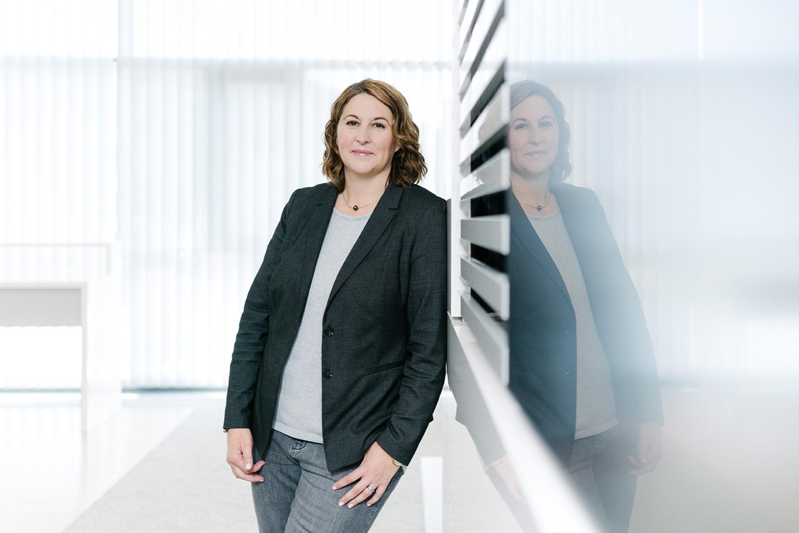 Alexandra lehnt sich an eine moderne Wand und lächelt in die Kamera