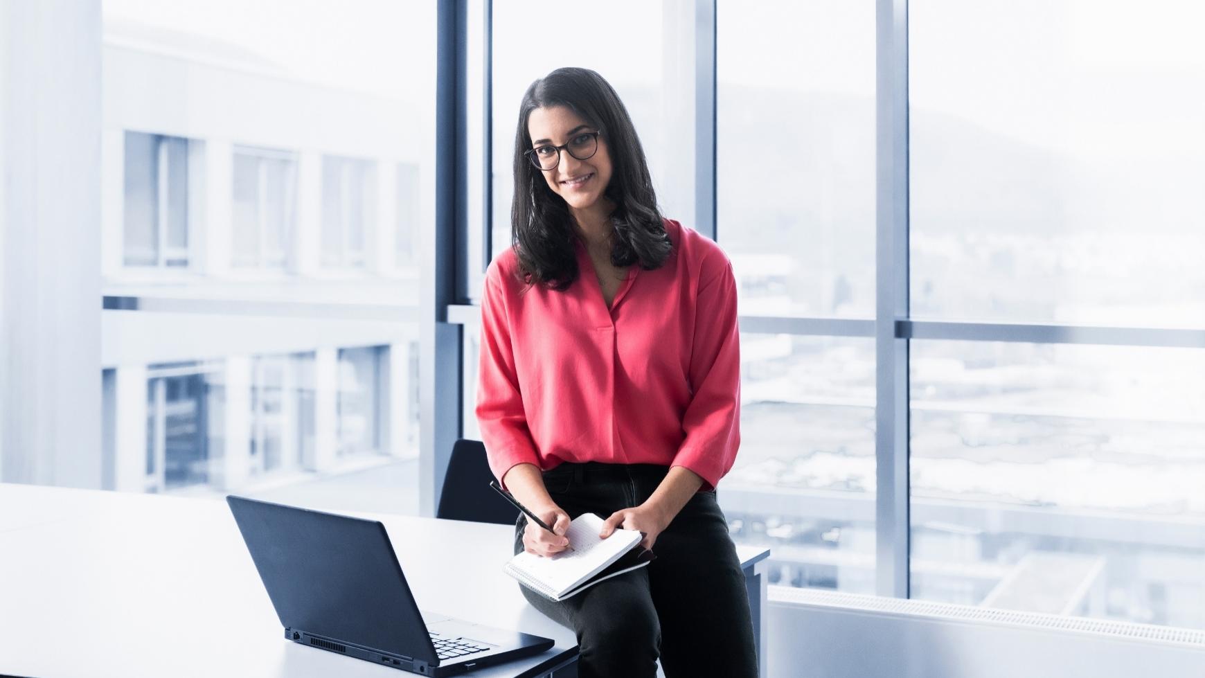 Camila in a modern office. She is making notes and looking warmly at the camera
