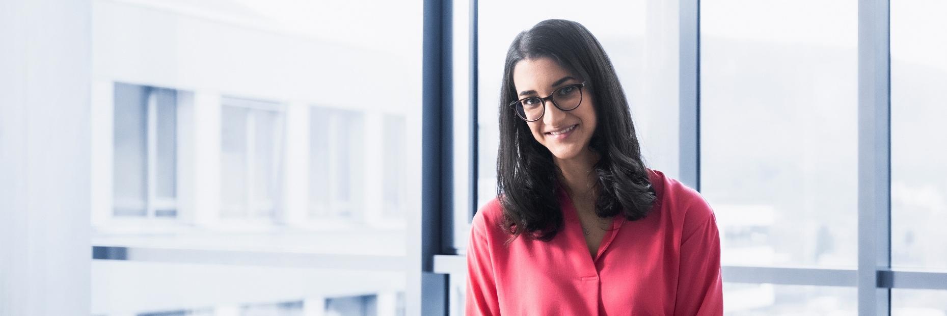 Camila in a modern office. She is making notes and looking warmly at the camera