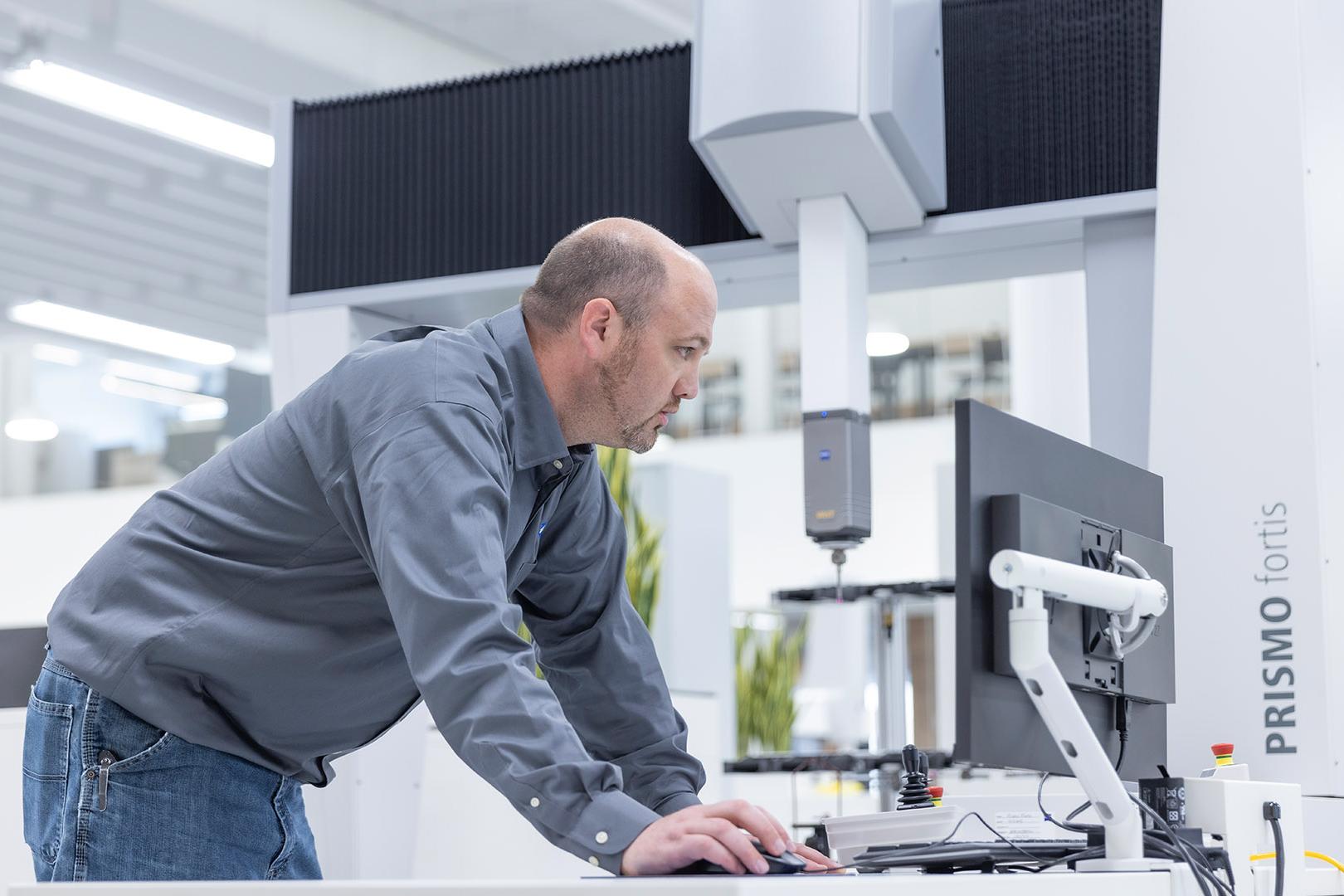 Jeff schaut auf den Computerbildschirm, während er neben dem hochpräzisen Koordinatenmessgerät (KMG) ZEISS PRISMO fortis steht.