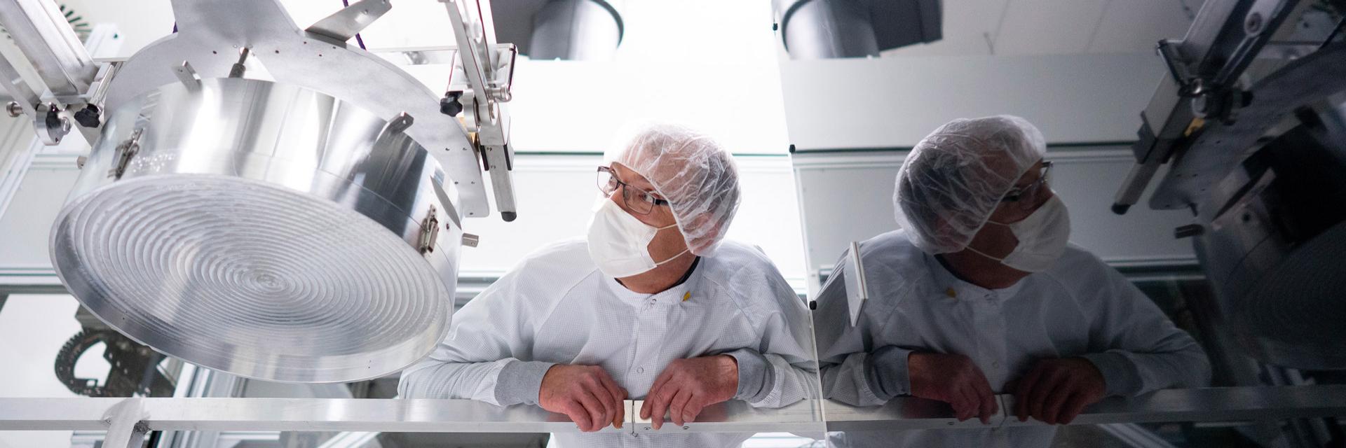 Close-up of a machine component for semiconductor manufacturing. Martin stands next to it in protective clothing and inspects it attentively