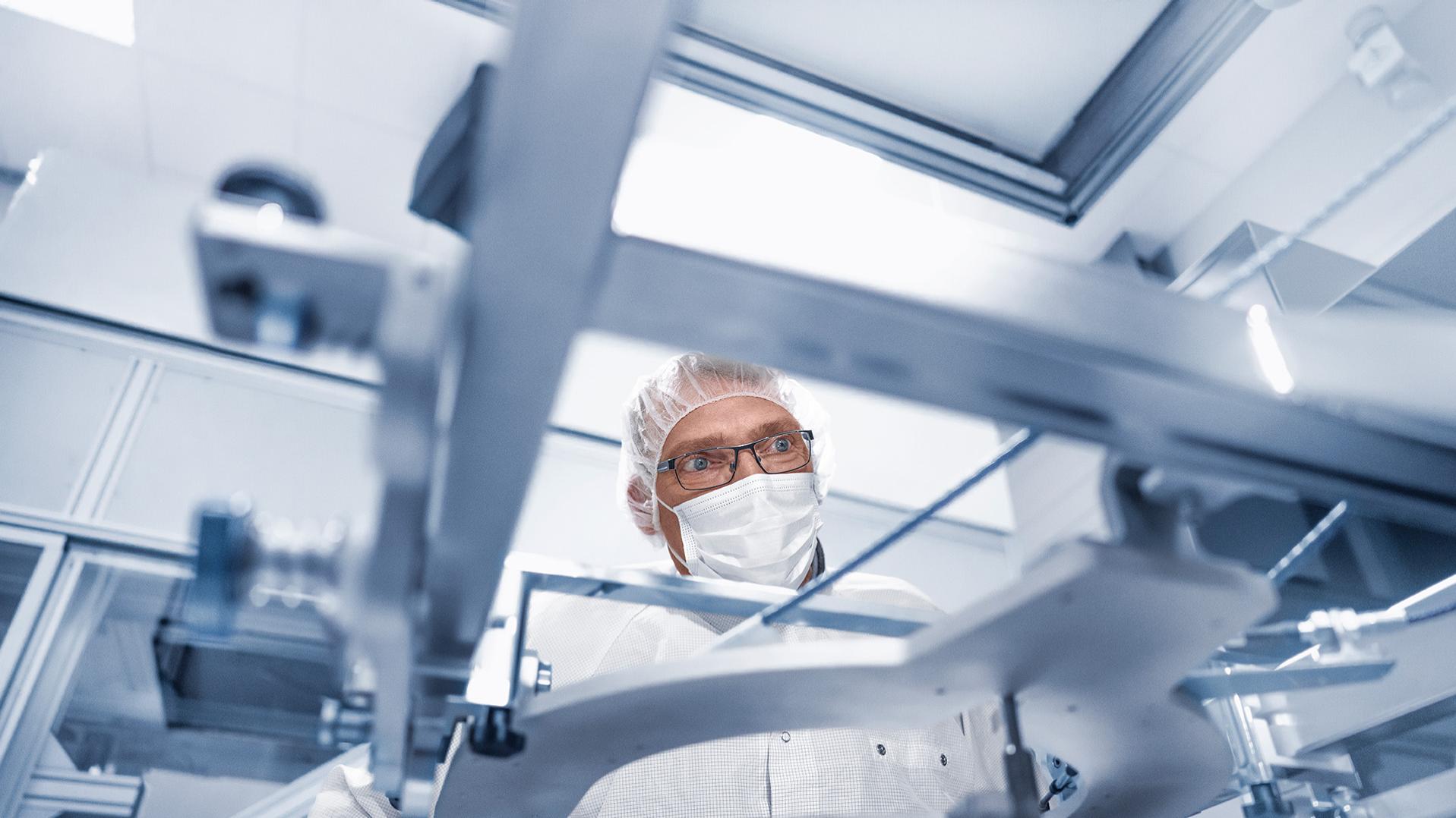 Martin in einer Schutzmaske, Haube und Brille bei der Arbeit in einer Fertigungshalle