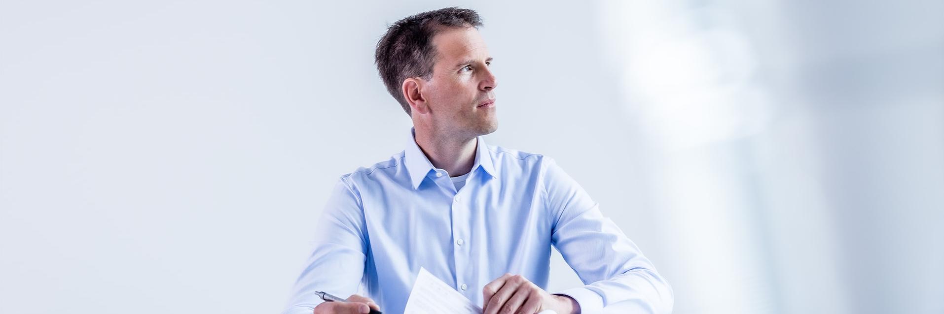 Felix writes on paper at a white desk and looks thoughtfully into the distance.