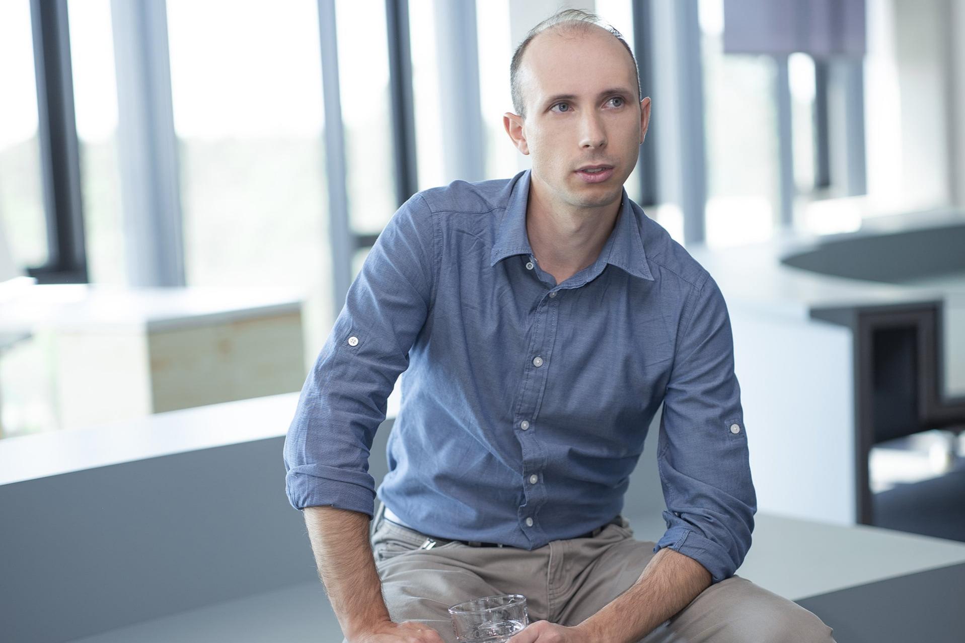 Guillaume sitzt auf einer Sitzbank im ZEISS Büro, trinkt ein Glas Wasser und spricht.
