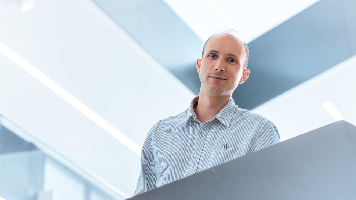 Guillaume walks down the stairs in the ZEISS office building, while looking at the camera and grinning happily